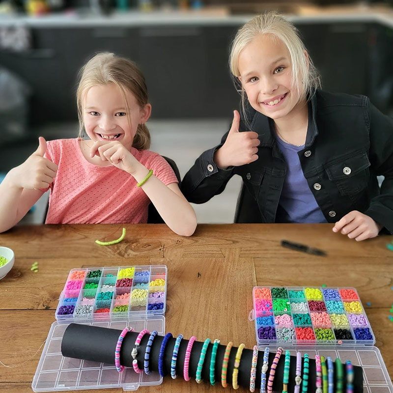 Isa en Sara, twee kinderen met hun duim omhoog met twee bakken gevuld met kralen om armbandjes te maken