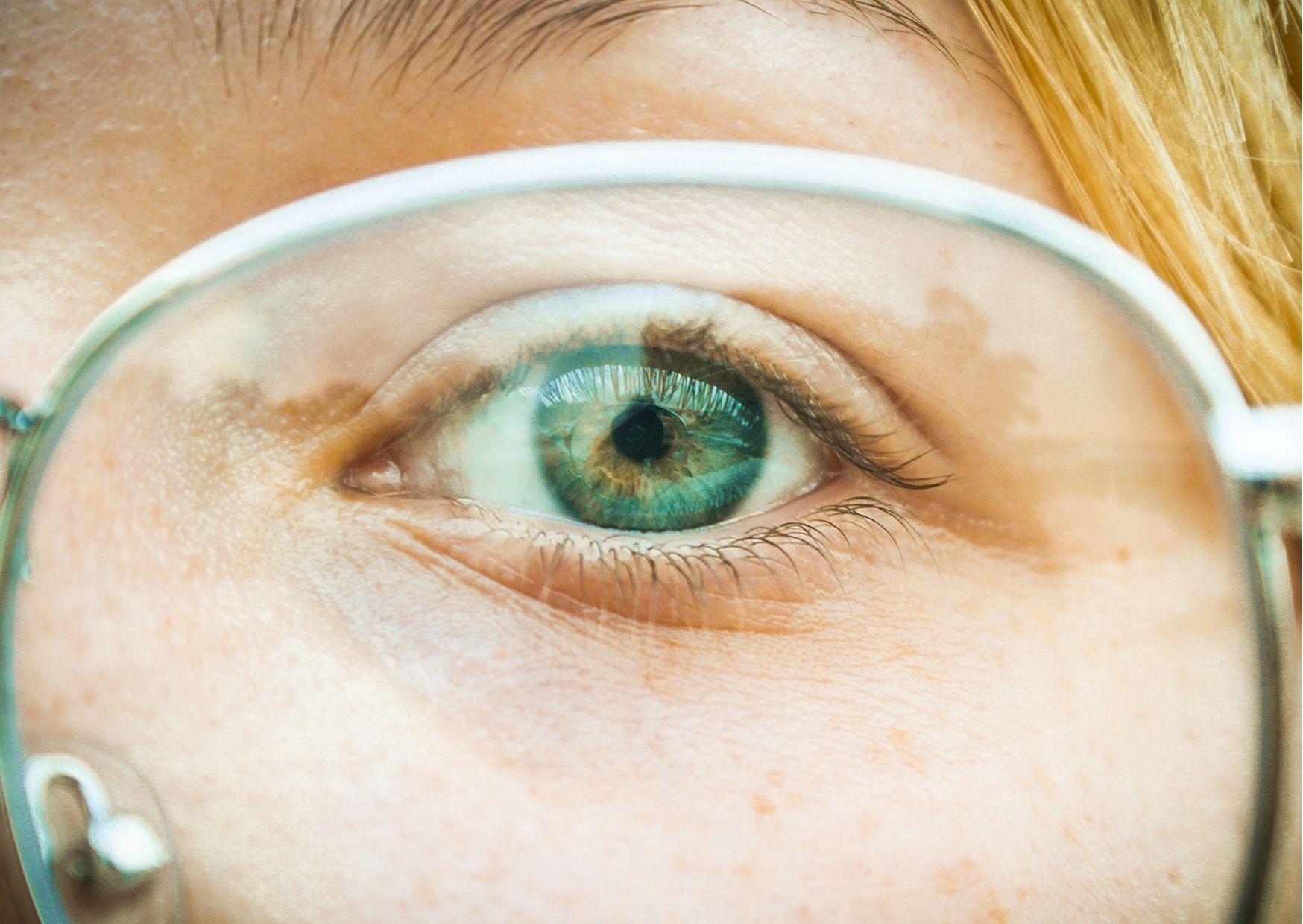 Een groen oog die door een bril kijkt.