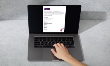 Laptop op een grijze tafel met een digitaal document op het scherm en een hand op het toetsenbord.