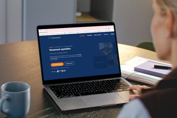 Persoon regelt online een testament via een laptop aan de keukentafel.